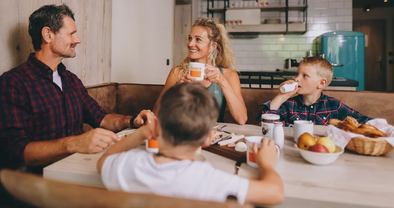 Familie sitzt gemeinsam am Tisch und genießt das Frühstück mit Essen und Getränken.