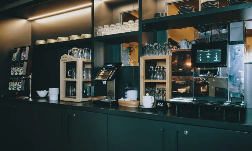 Moderne Bar mit Tee- und Kaffeemaschine, Gläsern und Geschirr auf Regalen