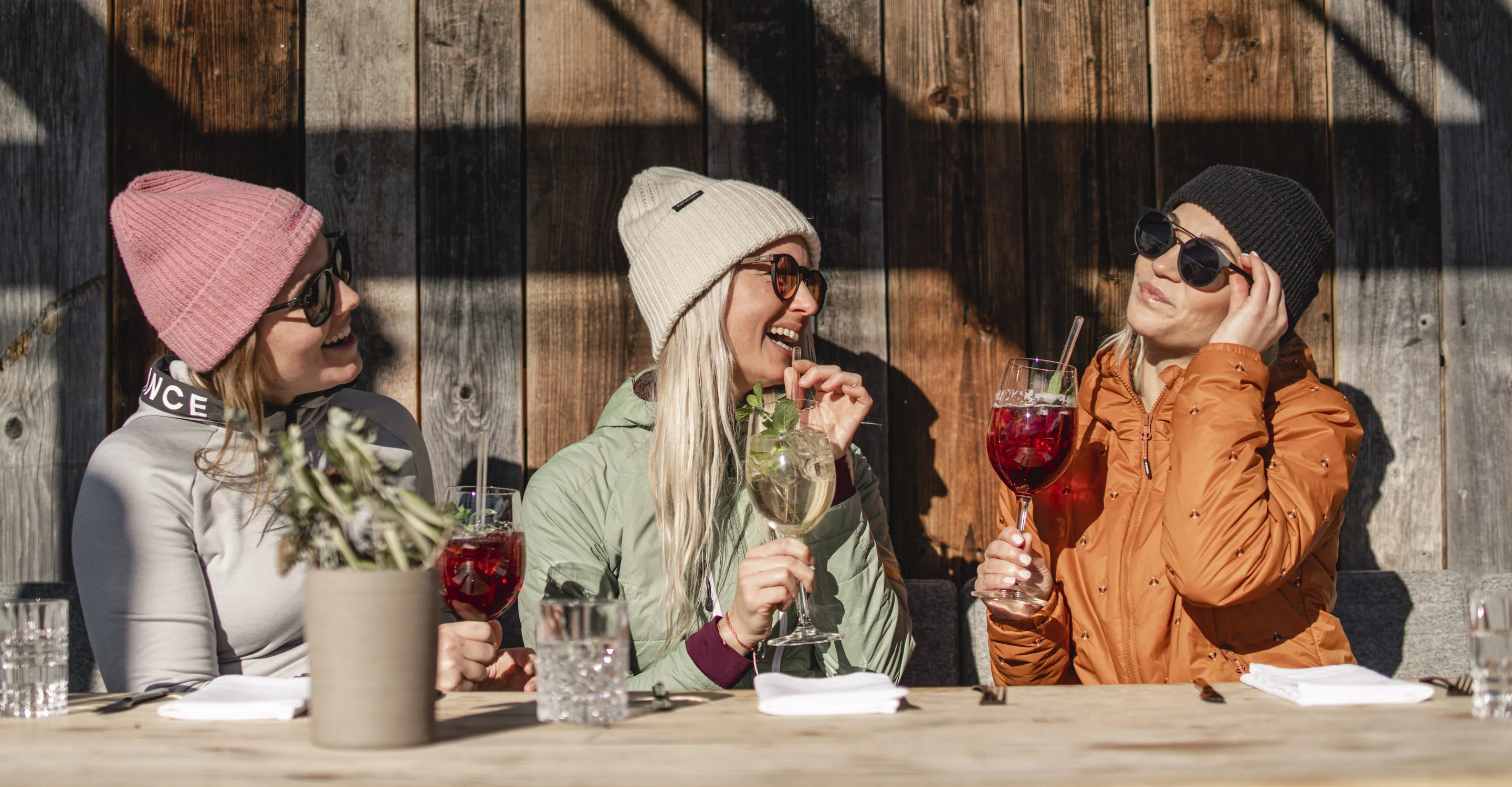Drei Frauen mit Getränken in der Hand sitzen an einem Tisch.