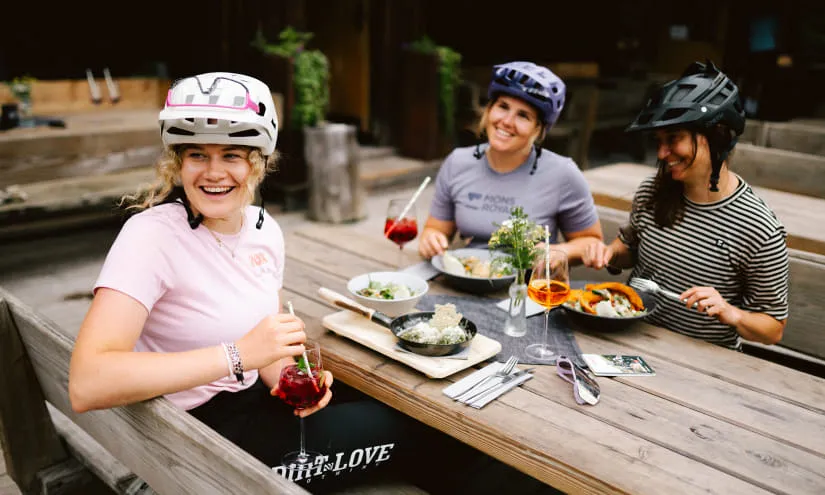 Drei Frauen in Fahrradhelmen sitzen an einem Tisch mit Essen.